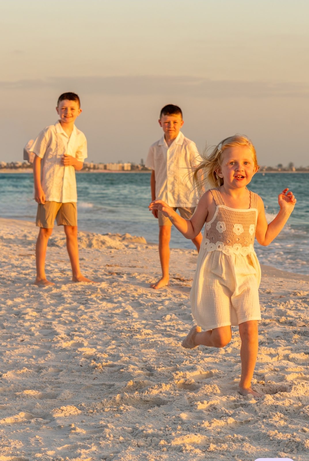 Three children playing on a sandy beach at sunset