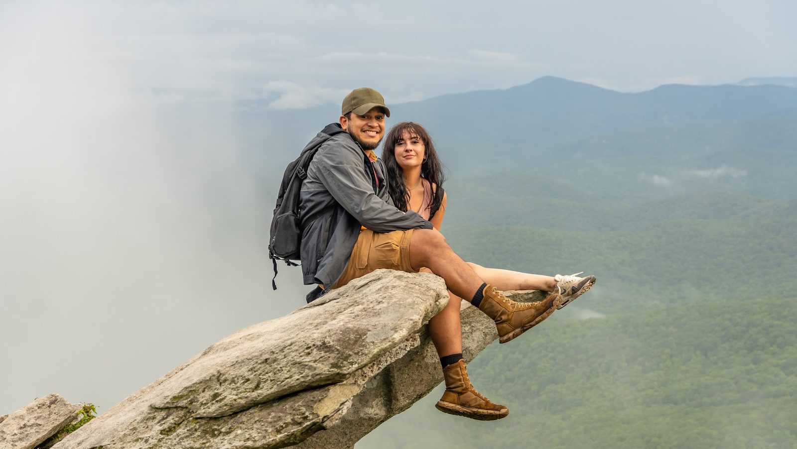 Couple sitting on cliff edge overlooking misty mountains