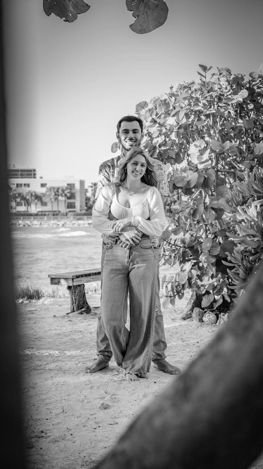Couple posing on beach with foliage and ocean background