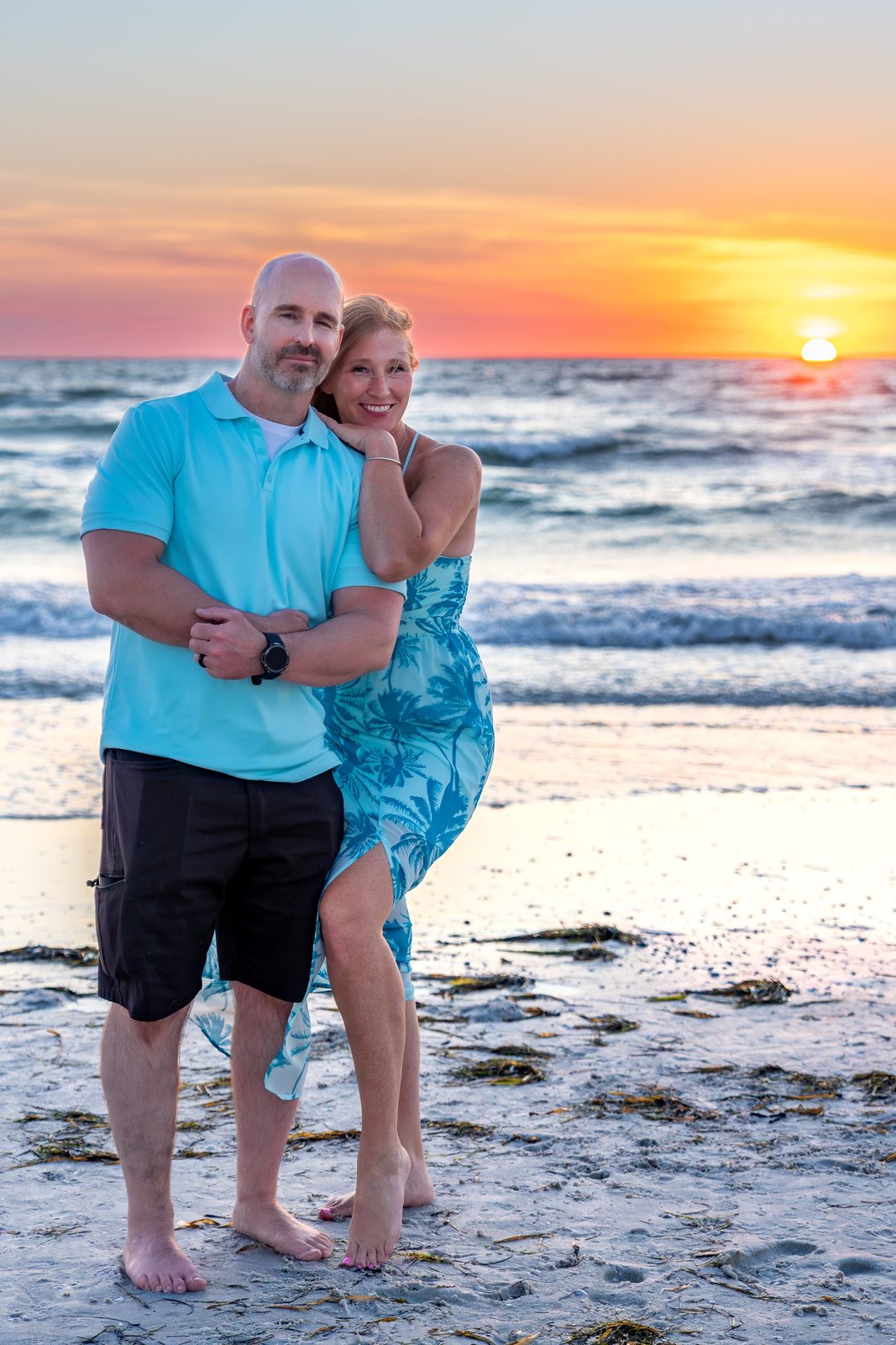 Couple posing on beach at sunset with ocean backdrop