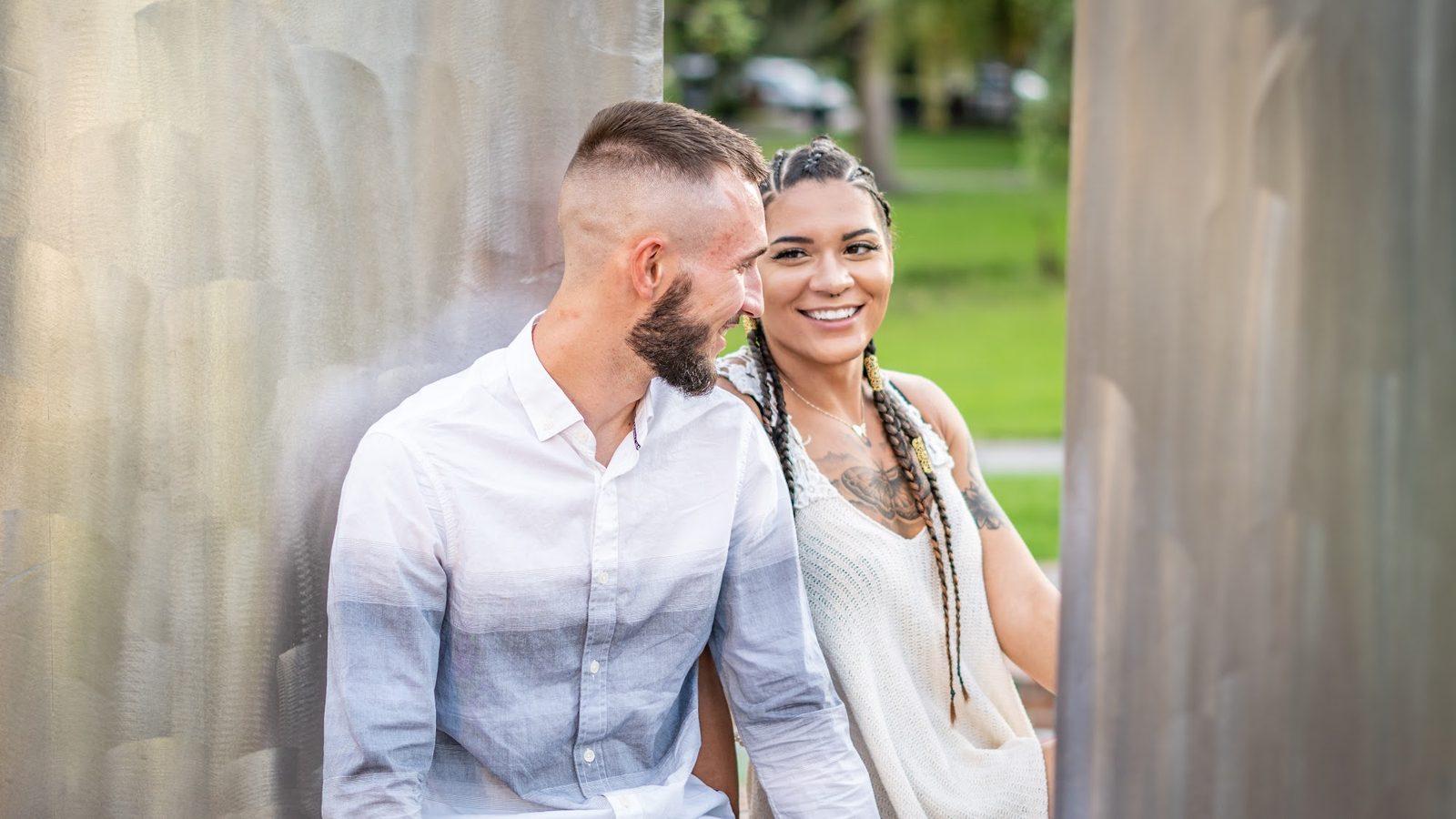 Couple standing outdoors near textured wall, smiling.
