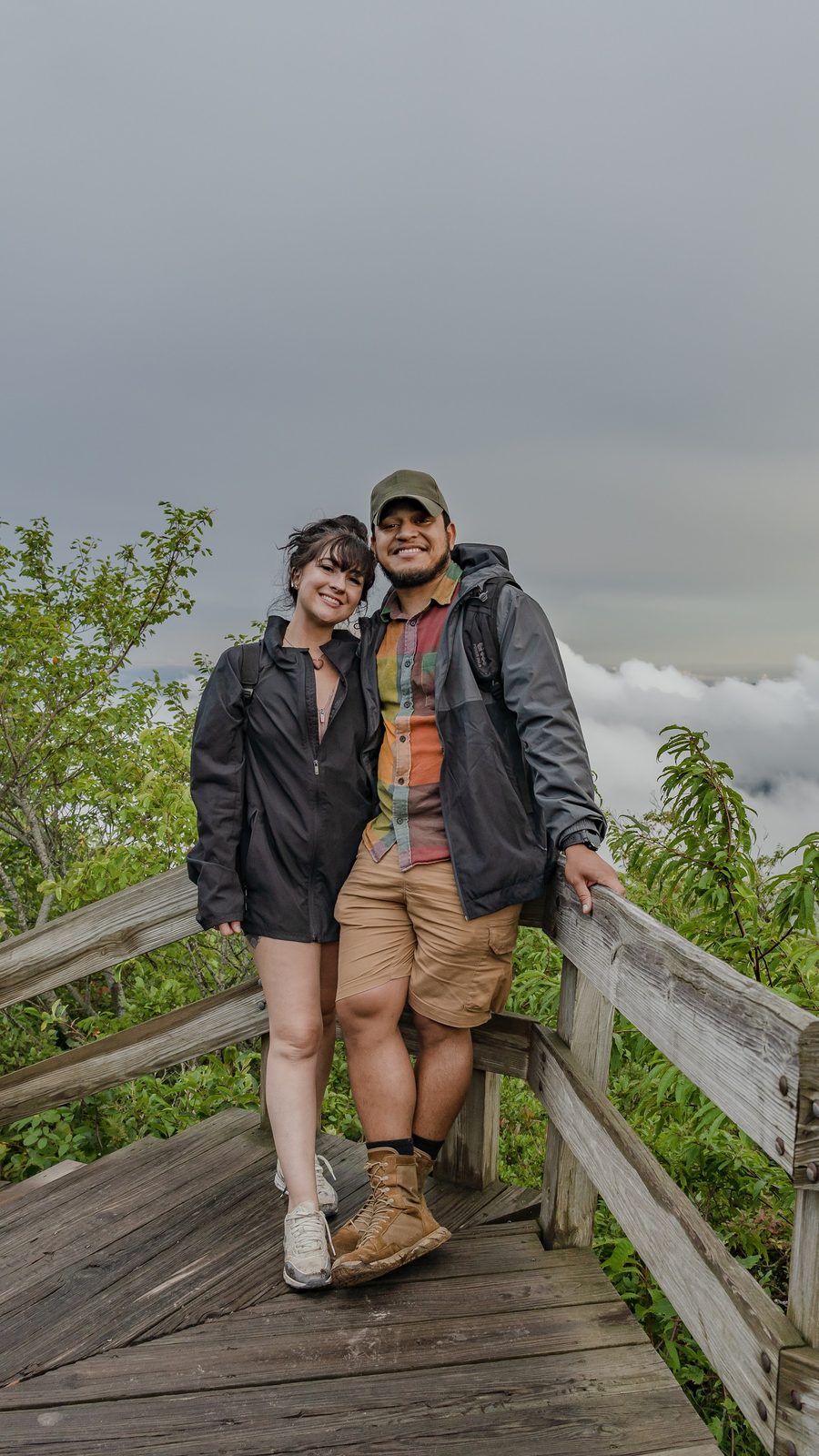 Two people posing on a wooden bridge with mountain clouds