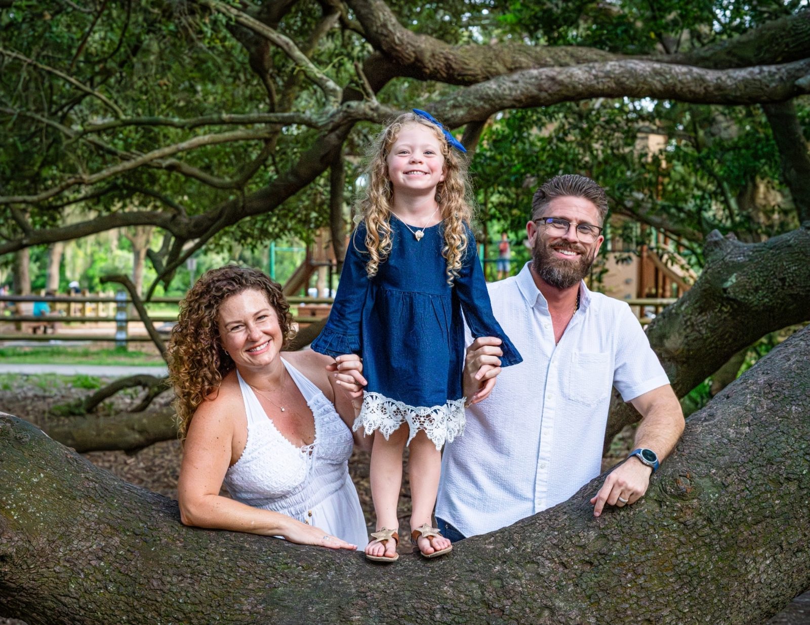 Family of three posing on tree branch in park