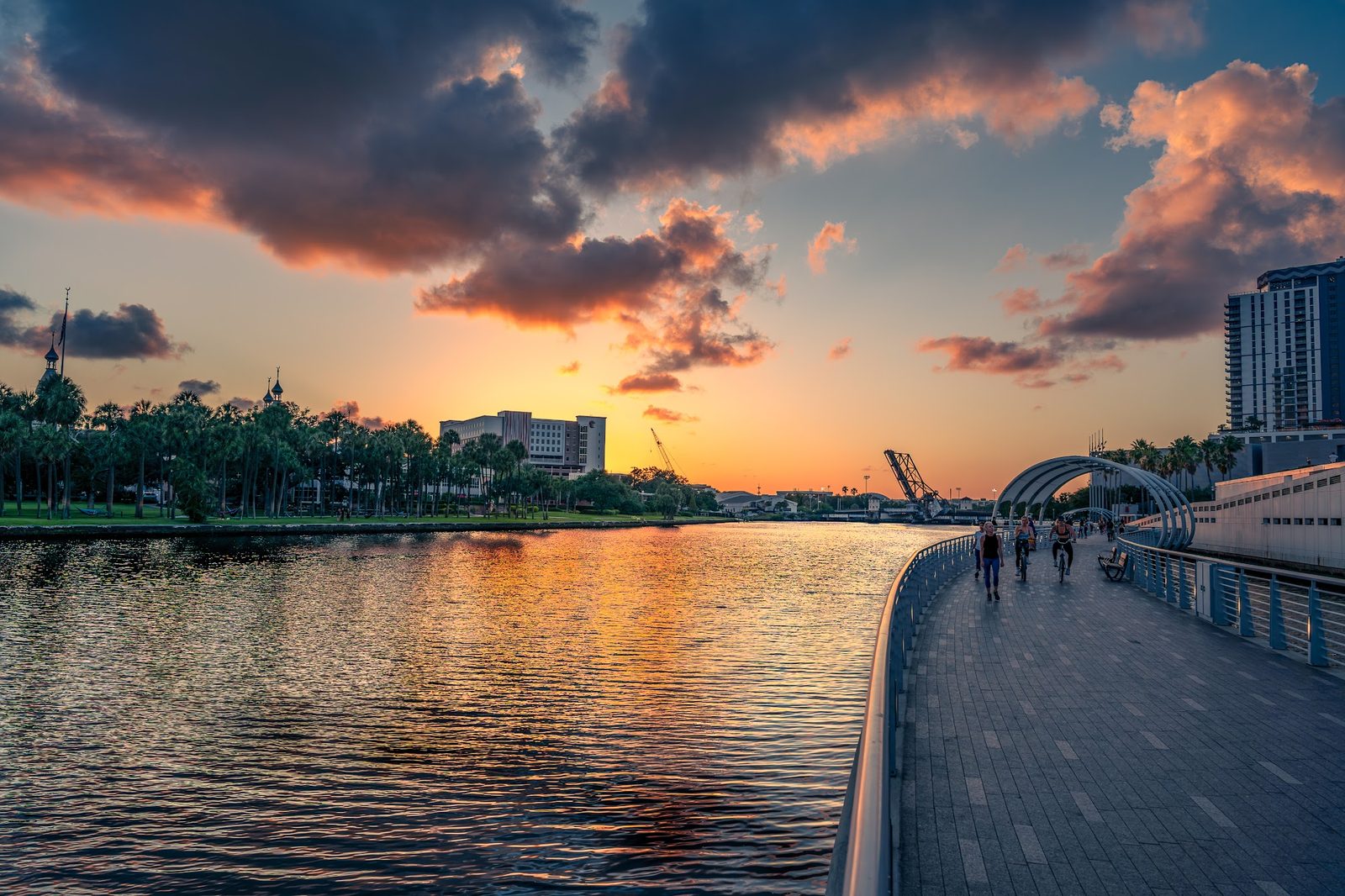 Sunset over waterfront with bridge, pedestrians, and city skyline