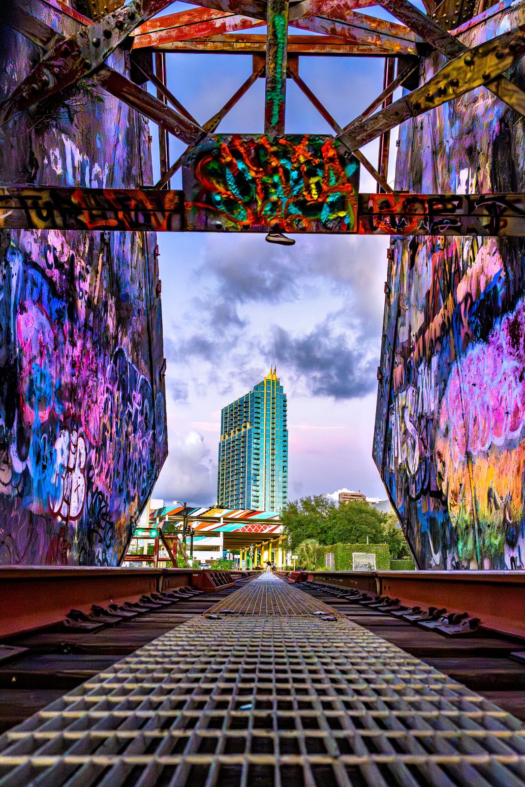 Graffiti-covered bridge with train tracks and city skyline