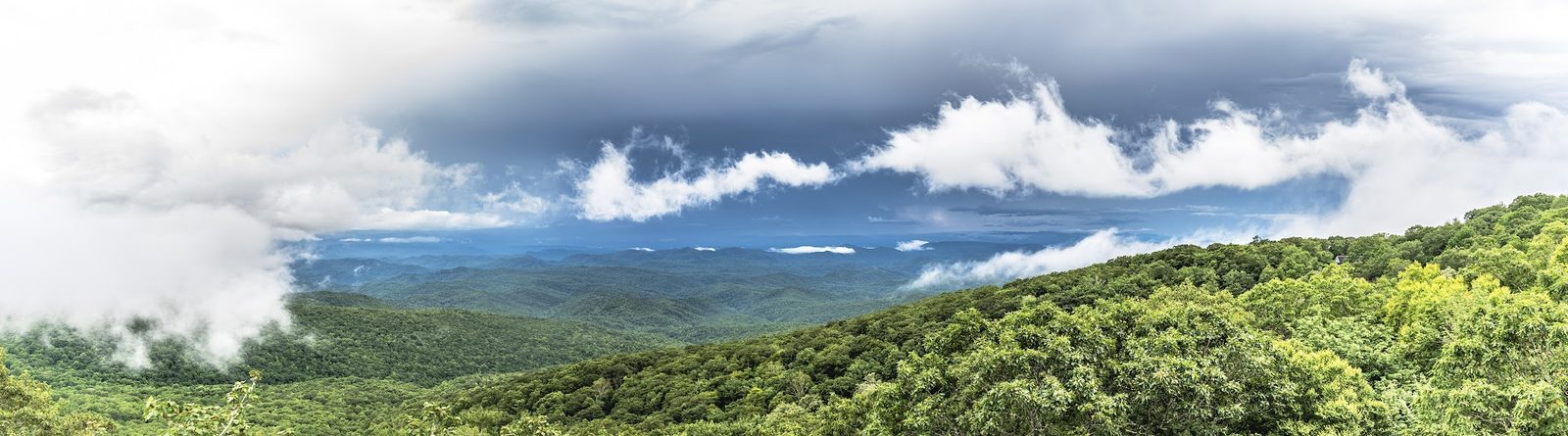 Landscape photo of mountainous forest with clouds and distant peaks