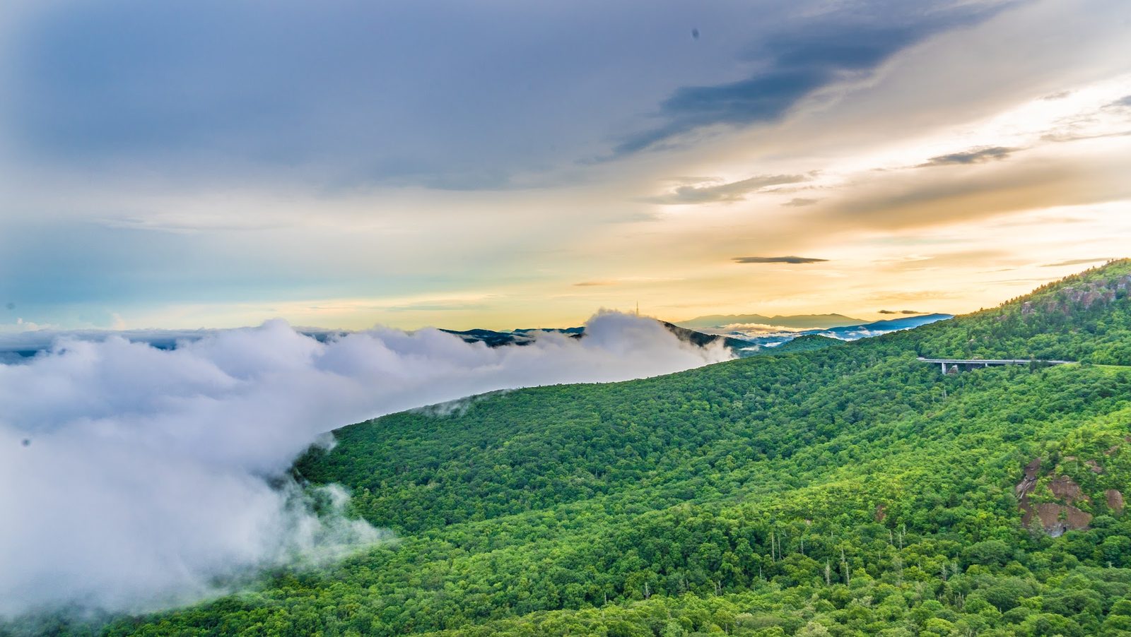 Landscape photo of green mountains, clouds, and sunset sky