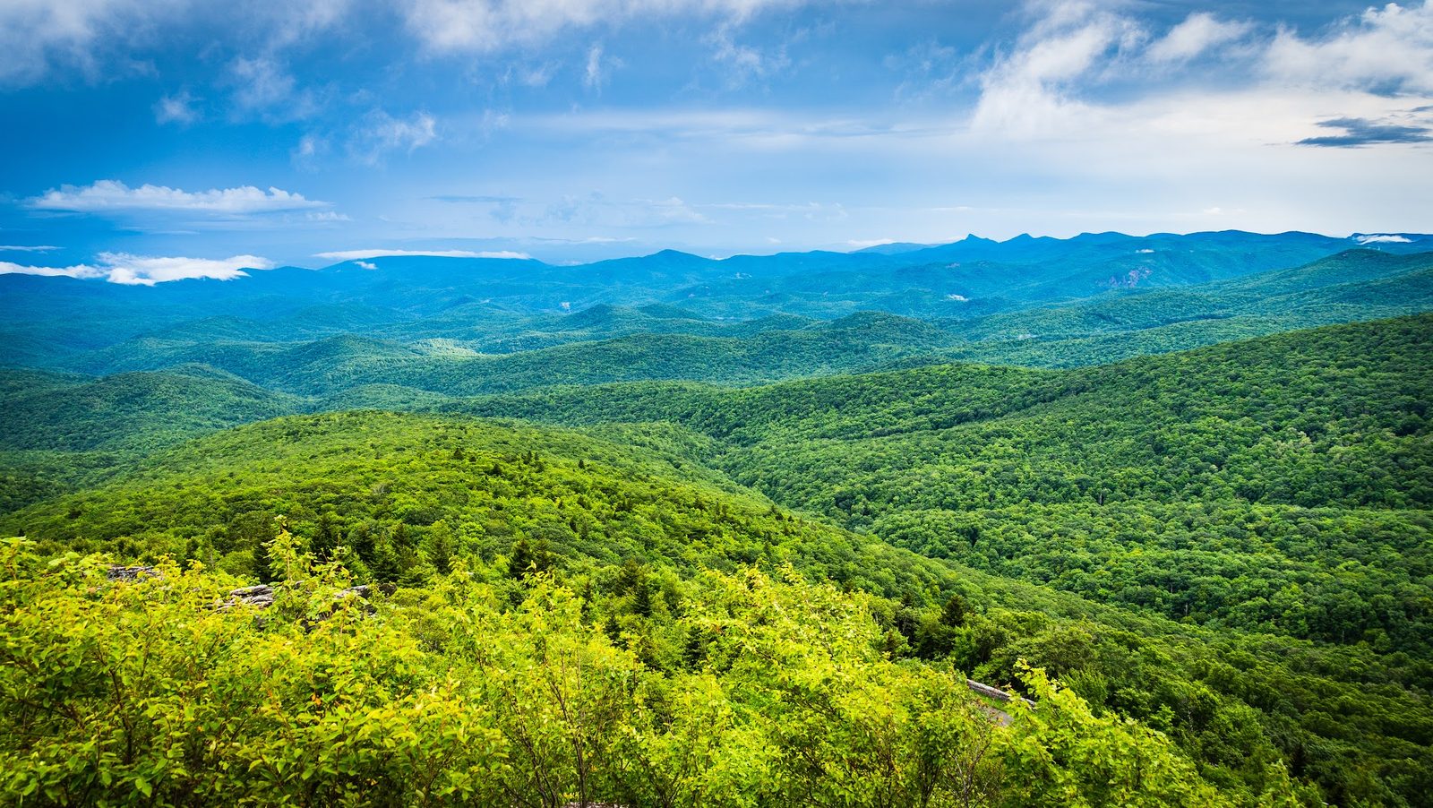 Lush green mountain range under blue sky with clouds