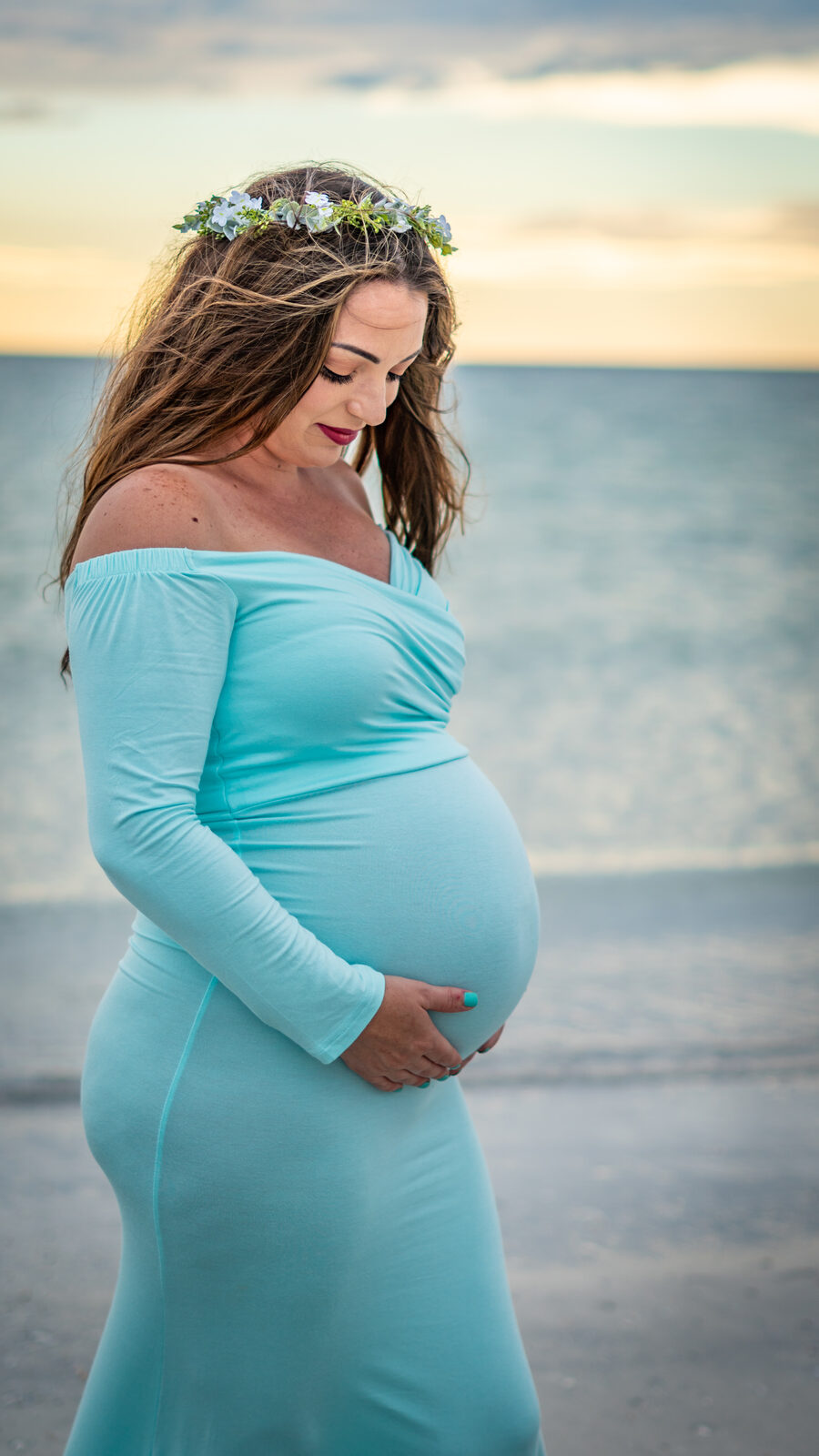 Pregnant woman holding belly on beach at sunset