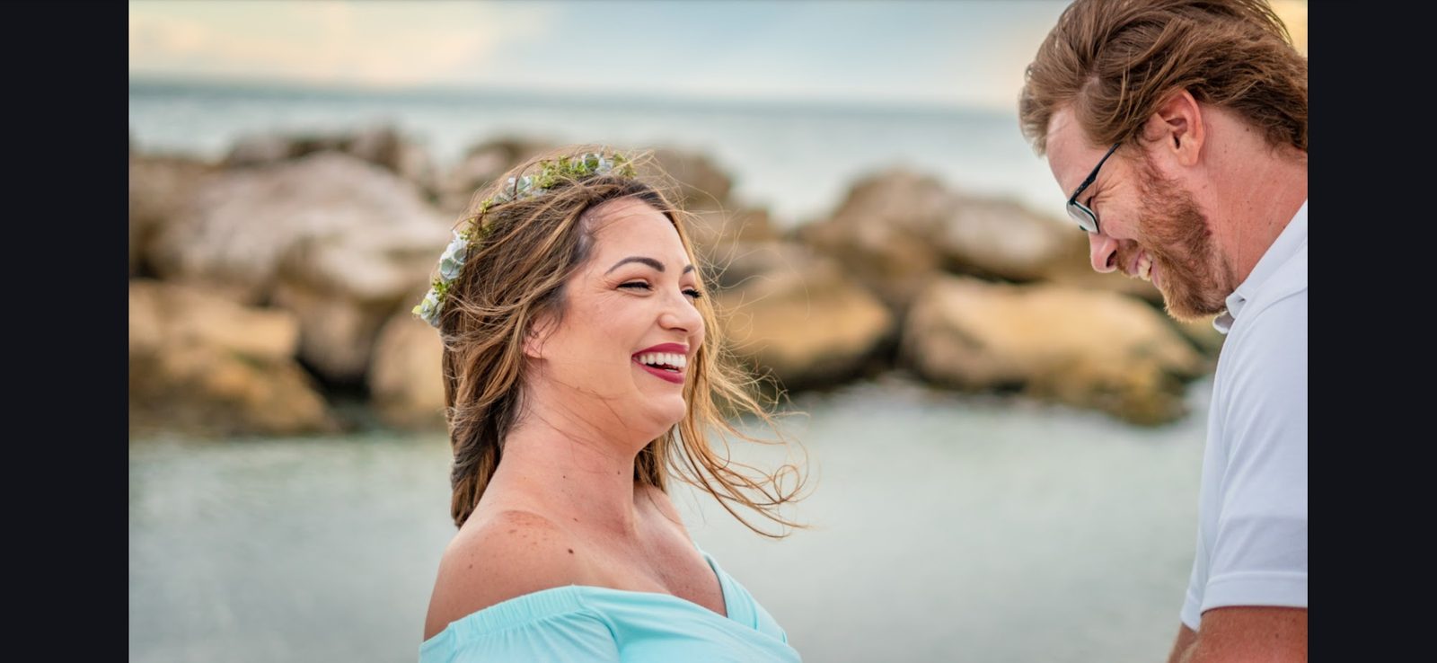 Couple smiling by sea with flower crown and rocks