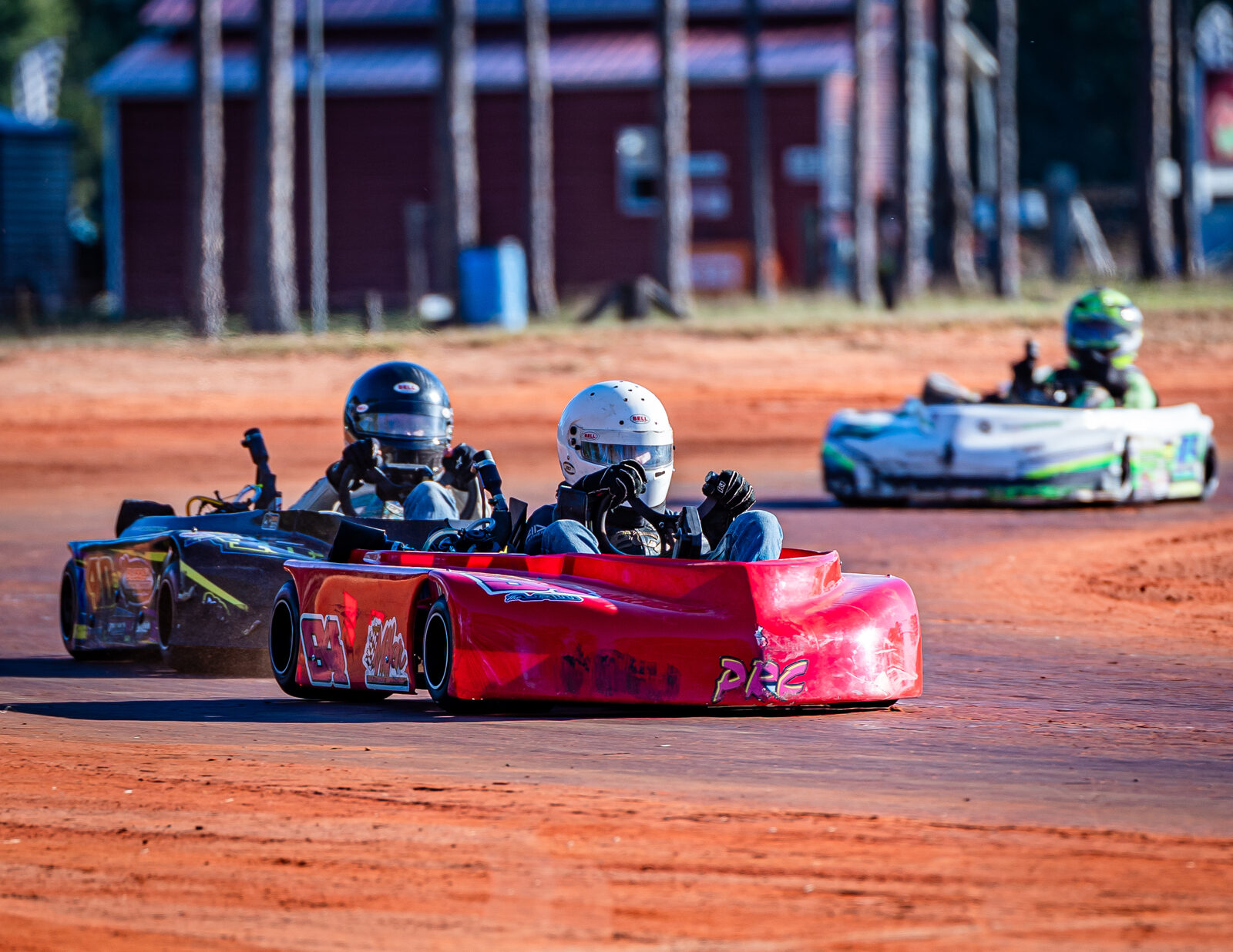 Go-karts racing on dirt track with drivers in helmets