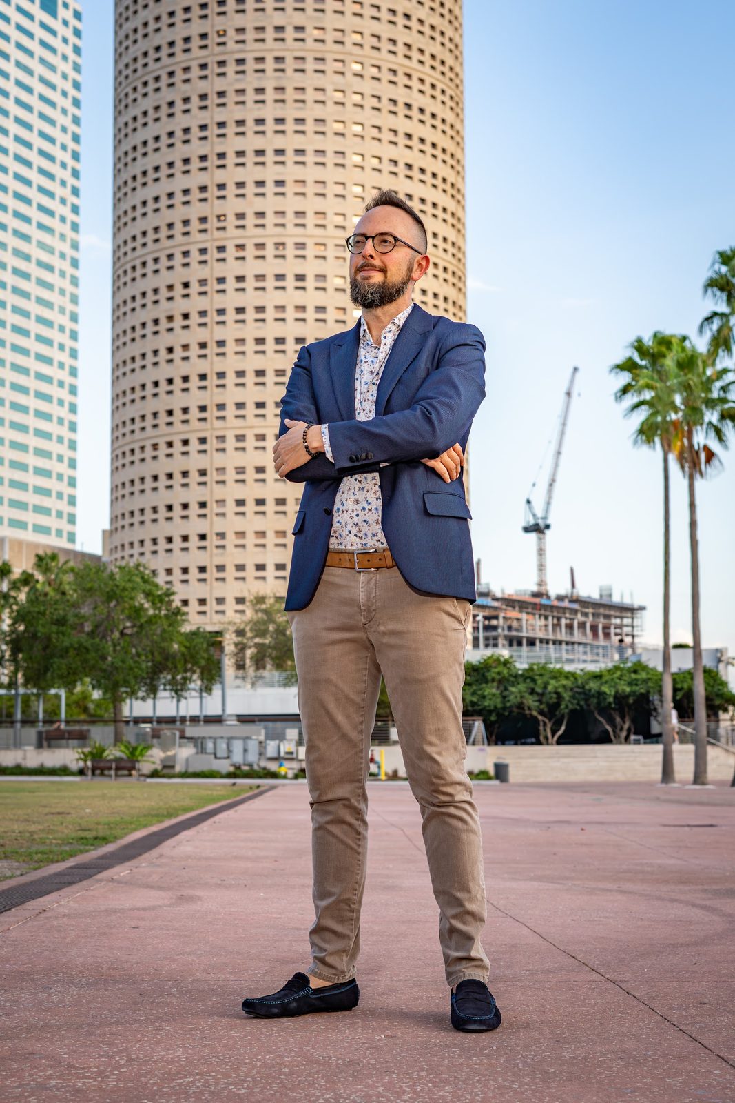 Man in blue blazer posing with arms crossed against city backdrop