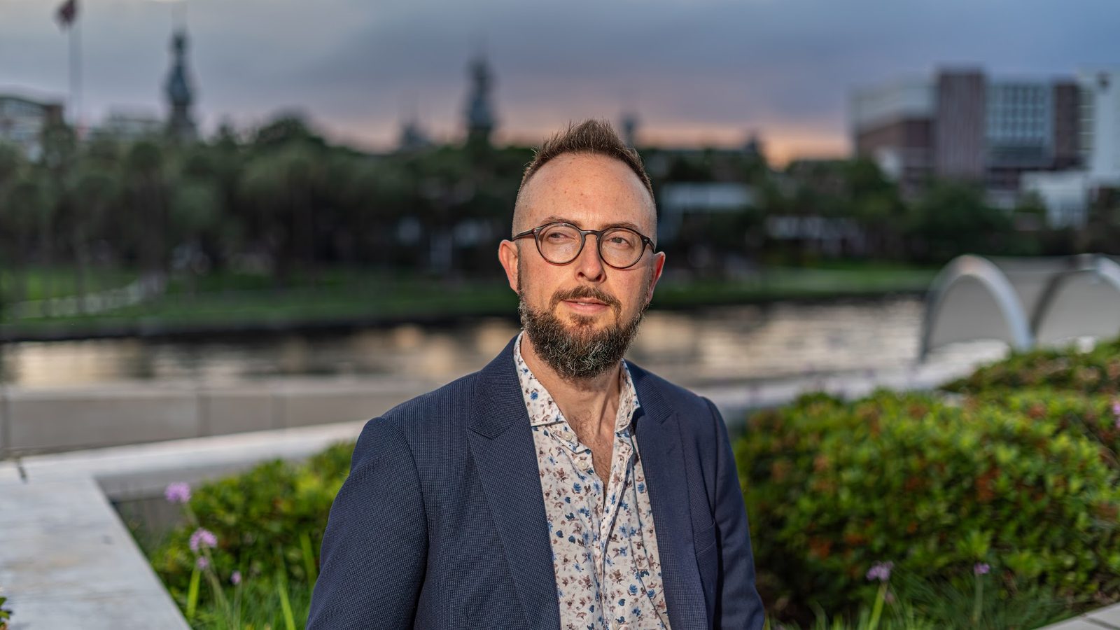 Man in suit and floral shirt posing outdoors with city background