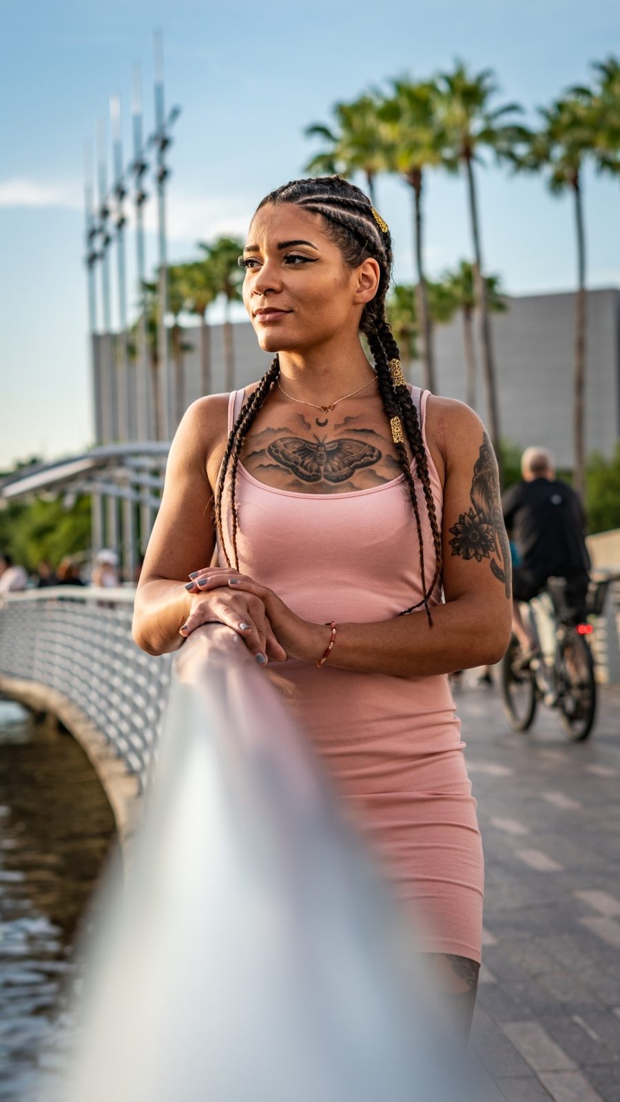 Woman in pink dress posing on bridge with tattoos and braids
