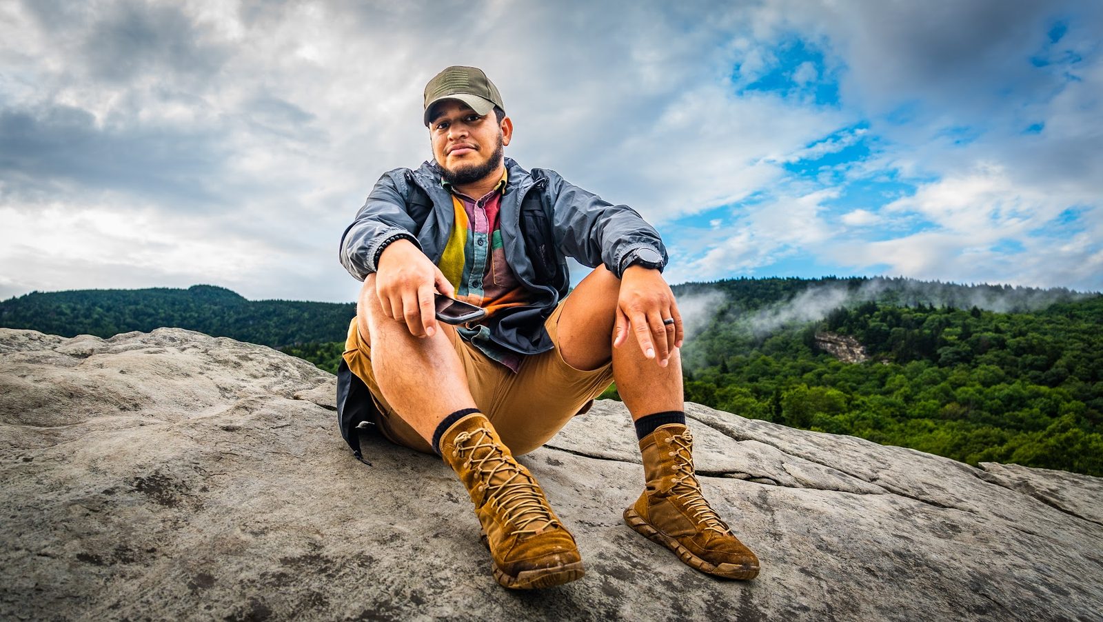 Man sitting on rock with forest and cloudy sky background