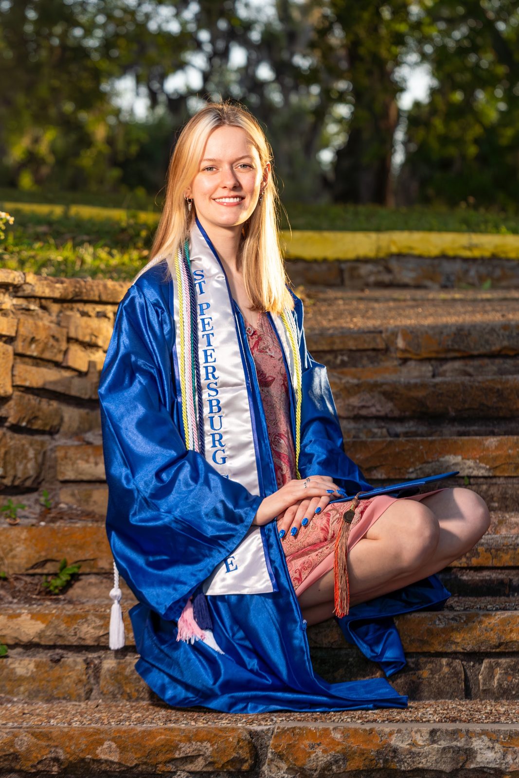 Graduation portrait of woman in blue gown on stone steps