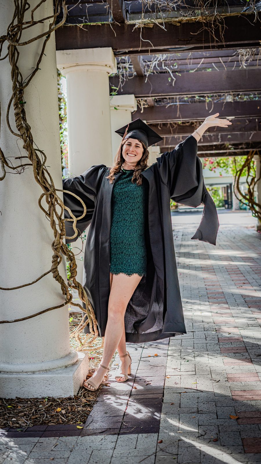 Graduate in cap and gown posing outdoors near columns