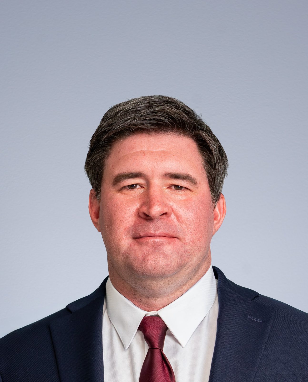 Headshot of a man in a dark suit and red tie