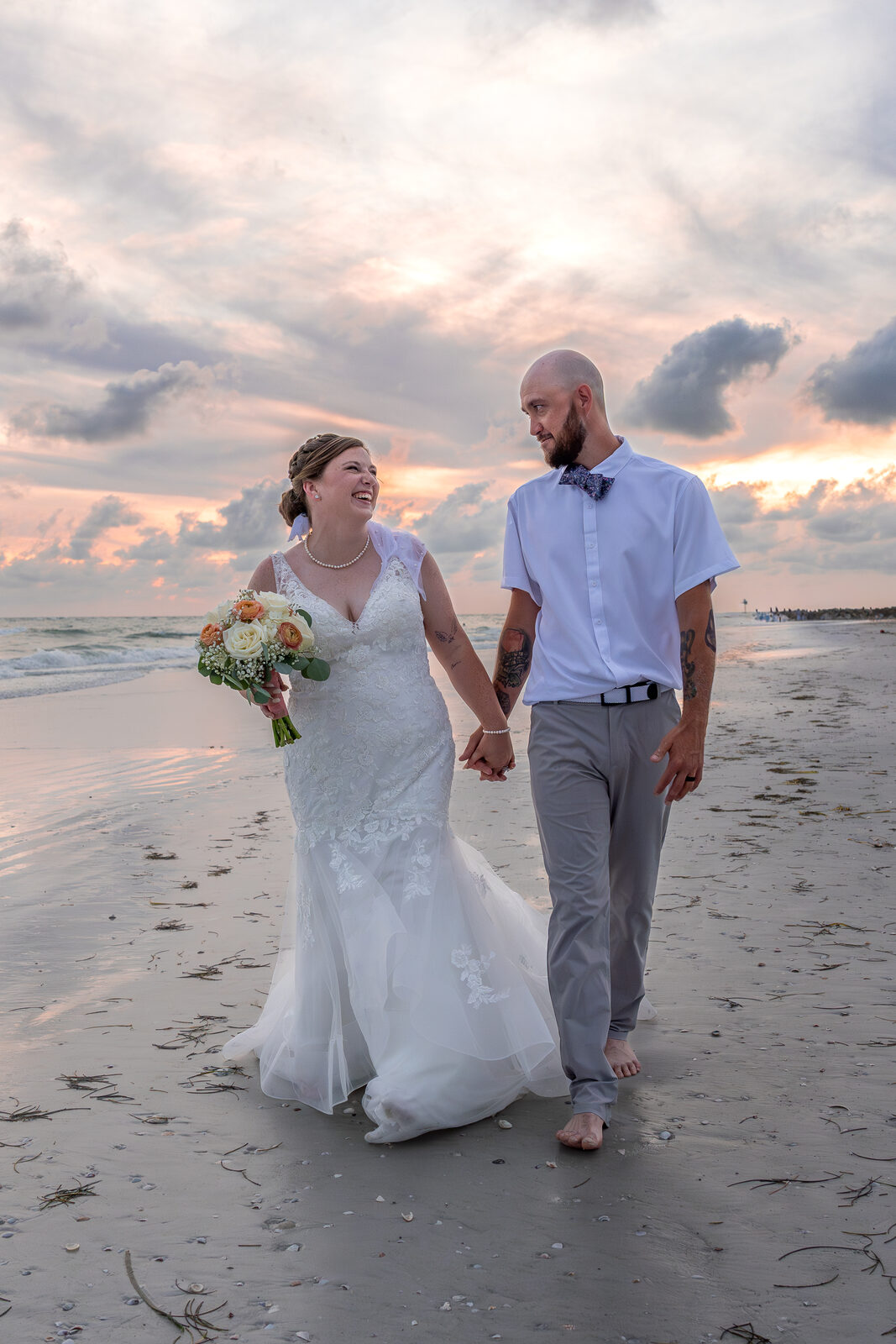 Bride and groom walking hand in hand on beach at sunset