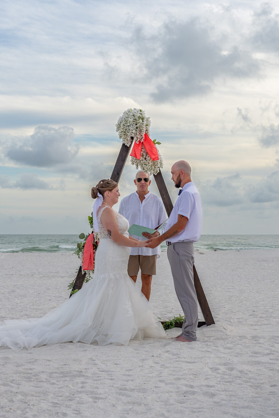 Bride and groom exchanging vows on beach with officiant