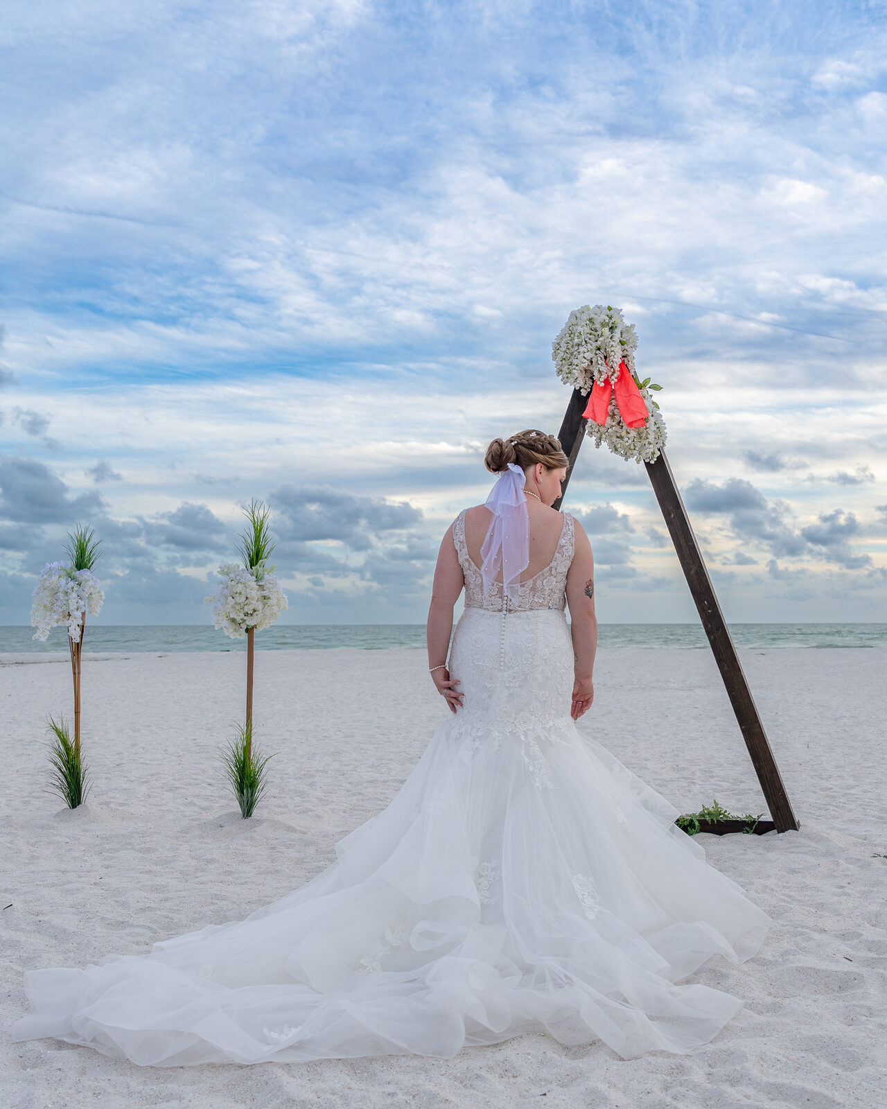 Bride in white gown on beach with floral arch