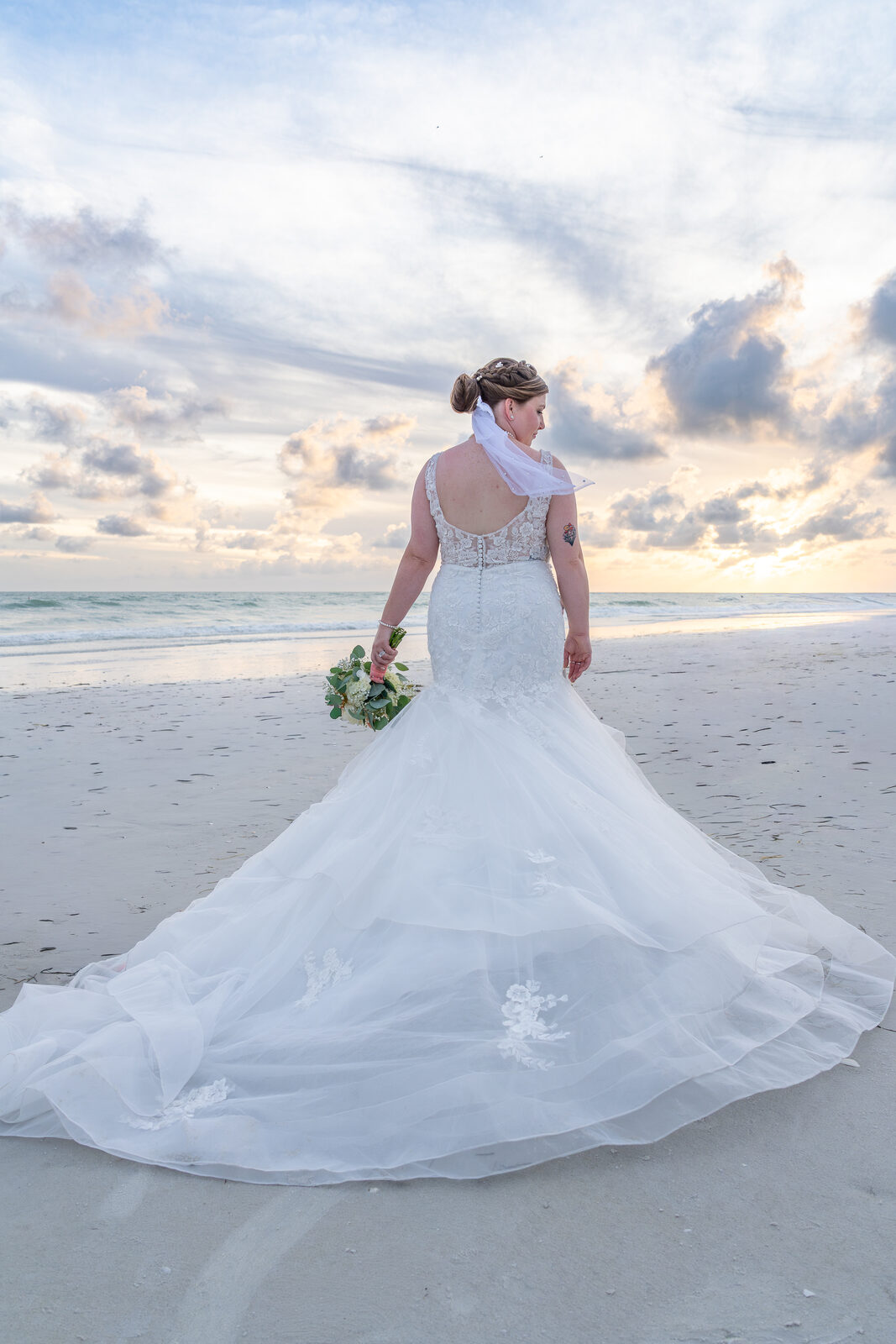 Bride walking on beach at sunset with bouquet