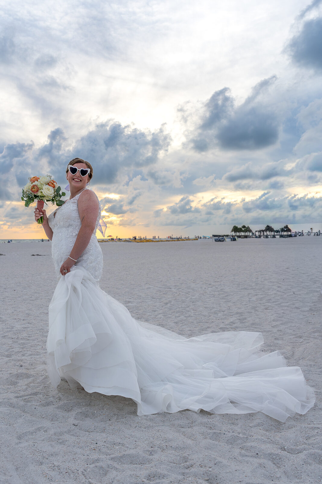 Bride in white gown holding bouquet on beach